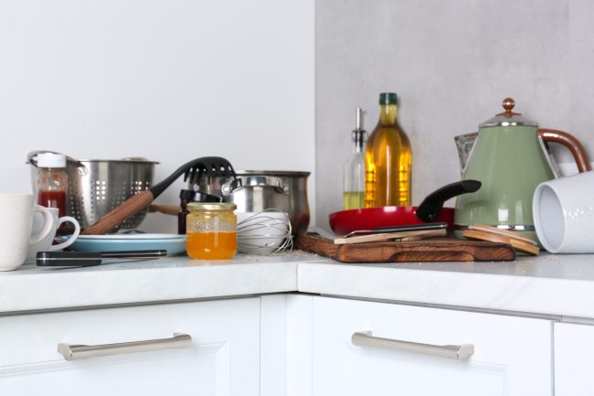 Many dirty utensils, cookware and dishware on countertop in messy kitchen